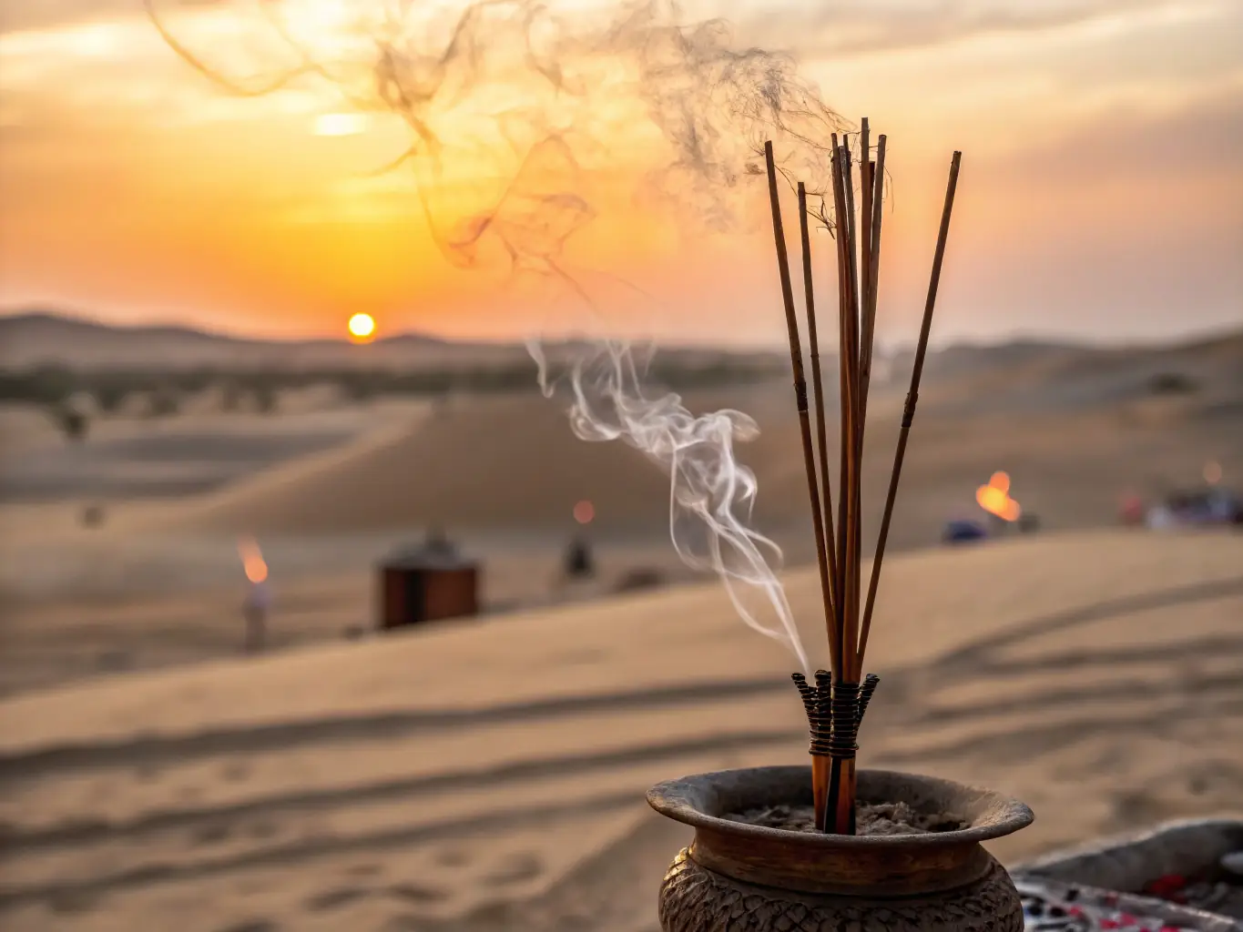 Close-up shot of 'Oud Al Sahra' incense sticks burning gently, releasing fragrant smoke. The background features a blurred desert landscape at sunset, evoking a sense of tranquility and Arabian heritage.
